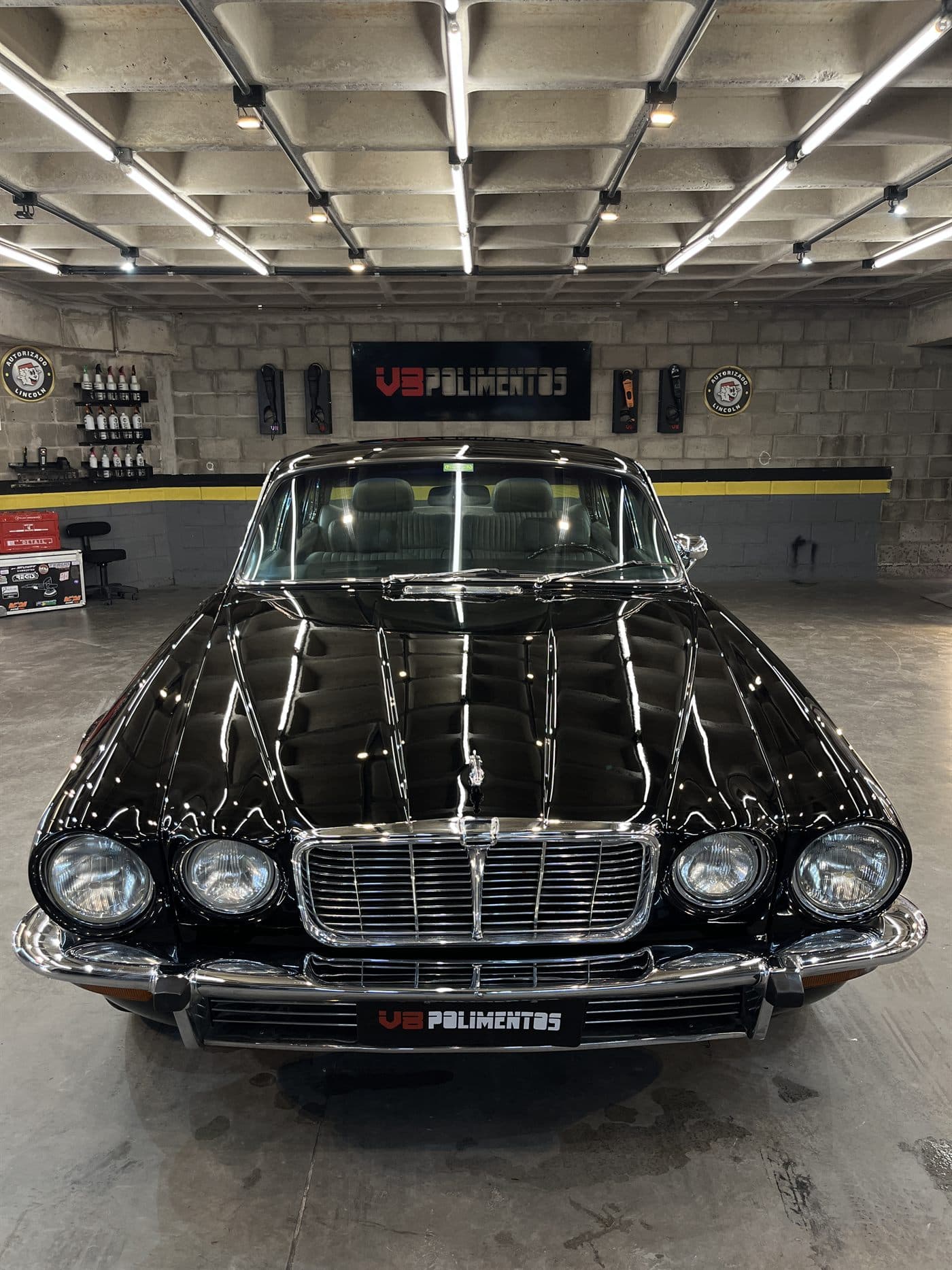 Jaguar preto recém-polido na oficina da V8 Polimentos, refletindo a iluminação do box